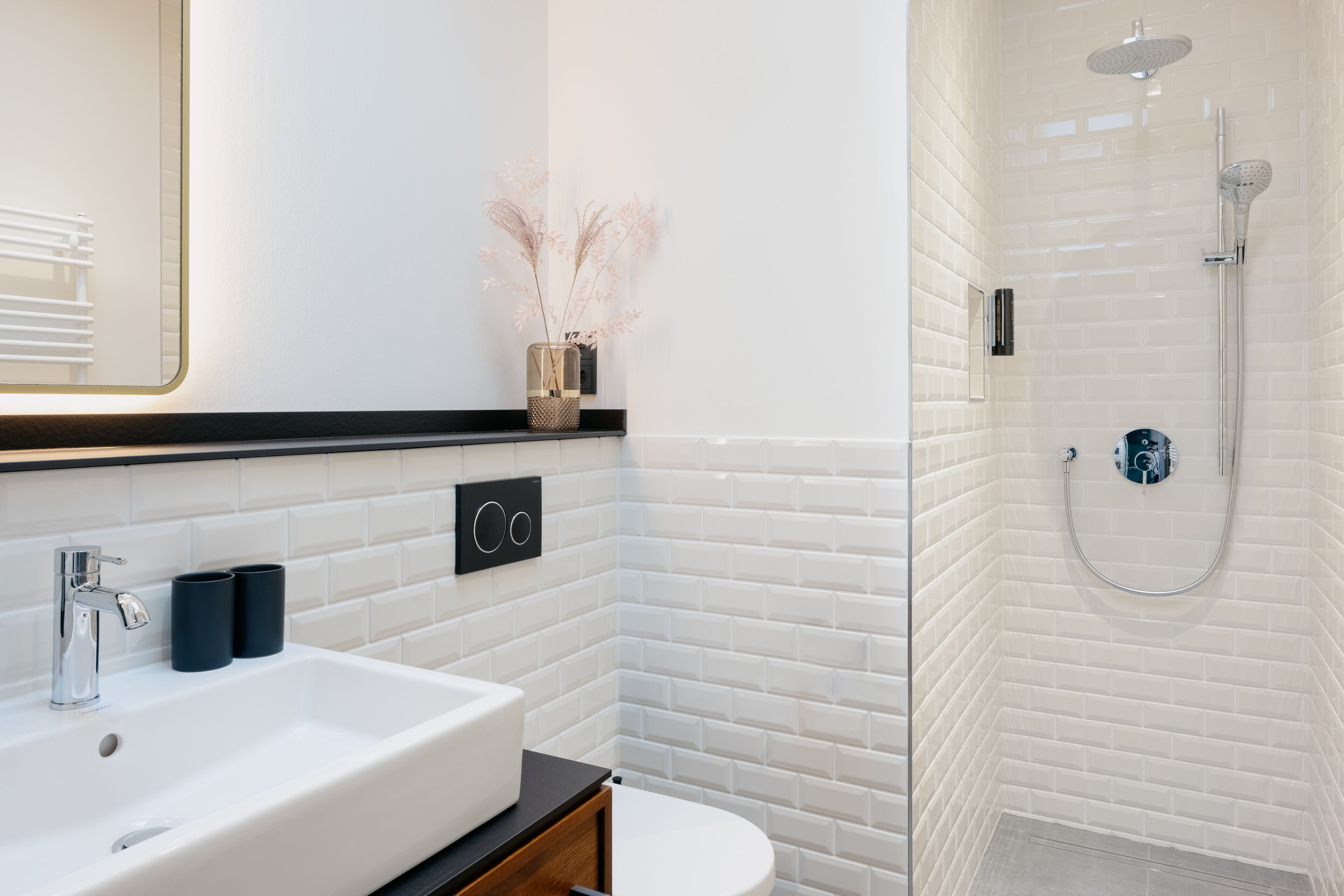 Un baño moderno con un lavamanos blanco, encimera negra y cabina de ducha con paredes de vidrio.