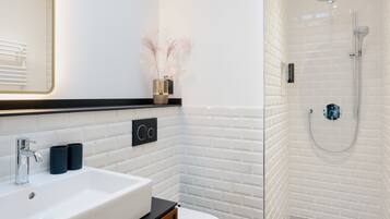 Un baño moderno con un lavamanos blanco, encimera negra y cabina de ducha con paredes de vidrio.