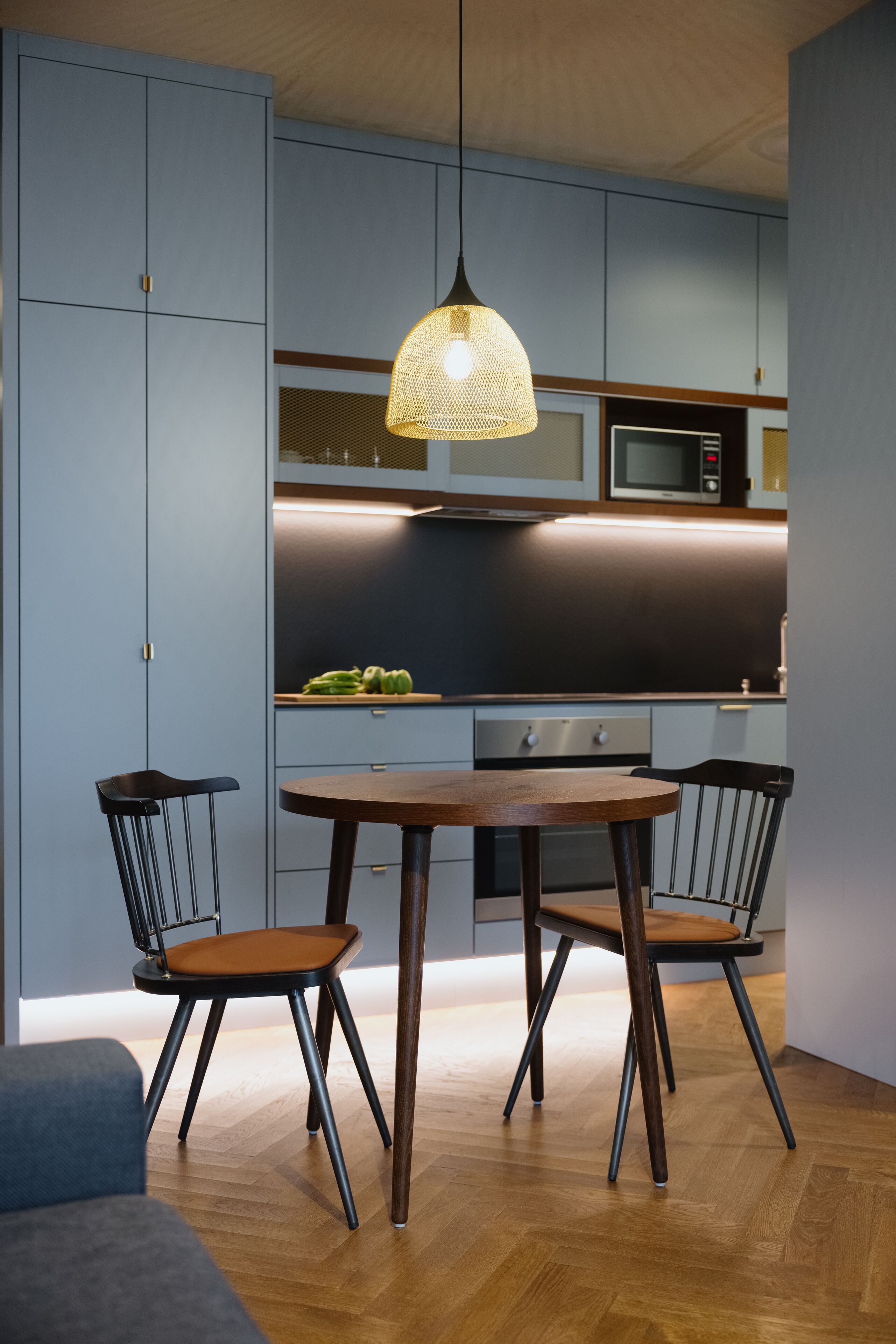 Una cocina moderna con una mesa redonda de madera y dos sillas, una lámpara colgante y electrodomésticos integrados.