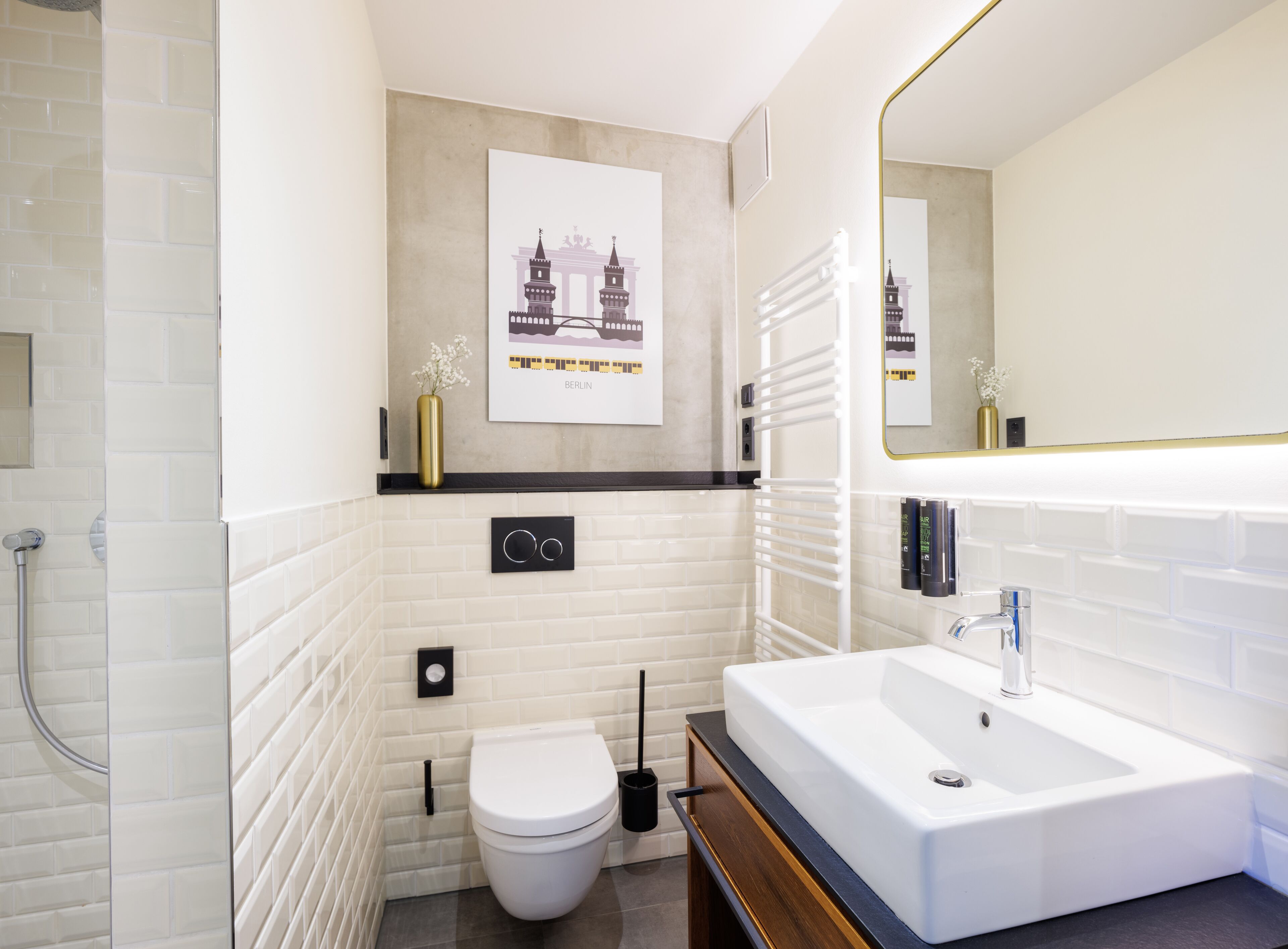A modern bathroom with a white subway tile wall, a large mirror, a white sink, and a toilet.