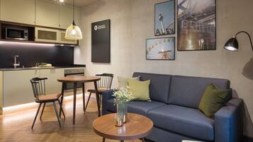 A modern living room with a sofa, a dining table, and chairs. There is a kitchen area with a microwave and a sink.
