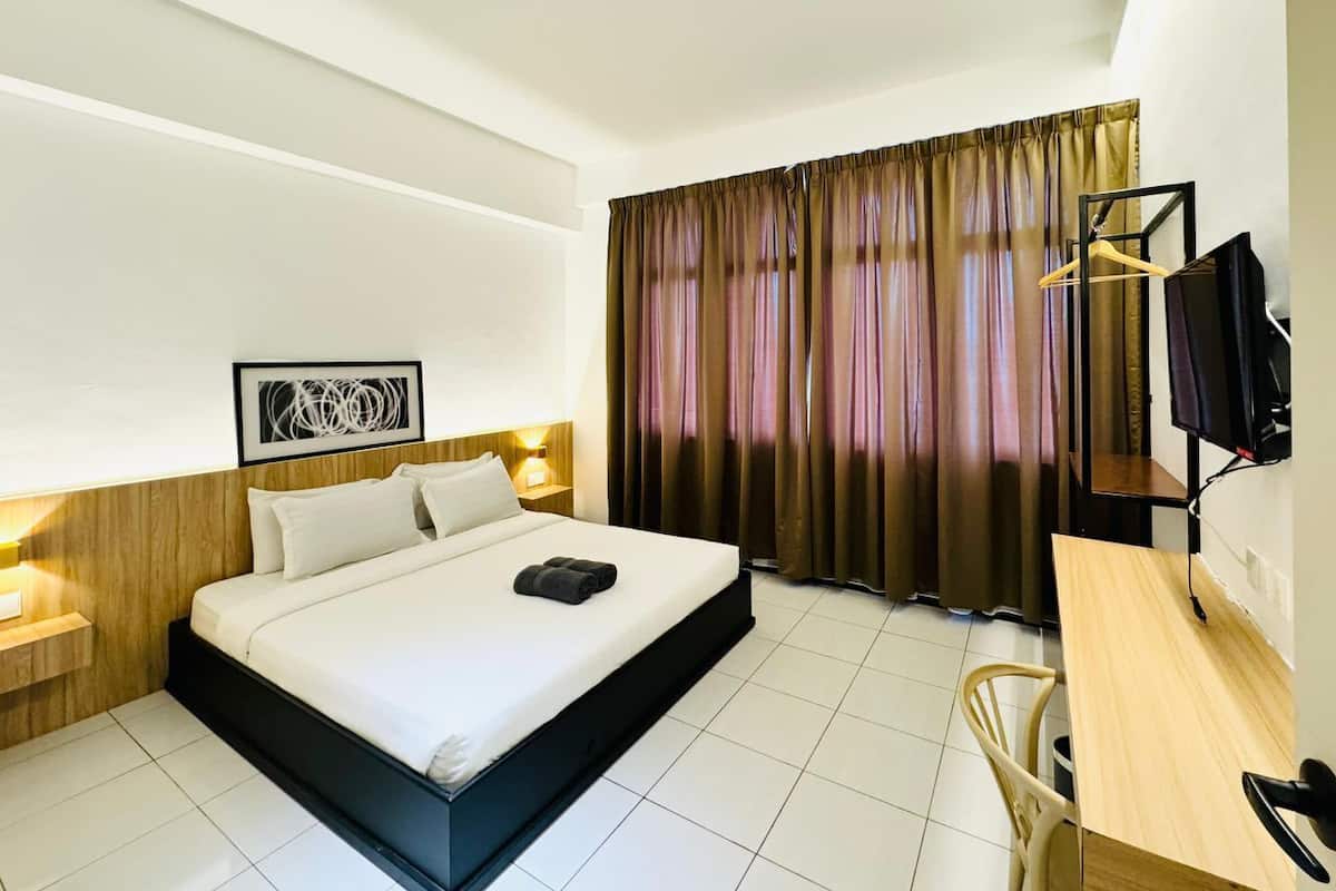 A hotel room with a bed, bedside tables, a desk, a chair, a television, and curtains.