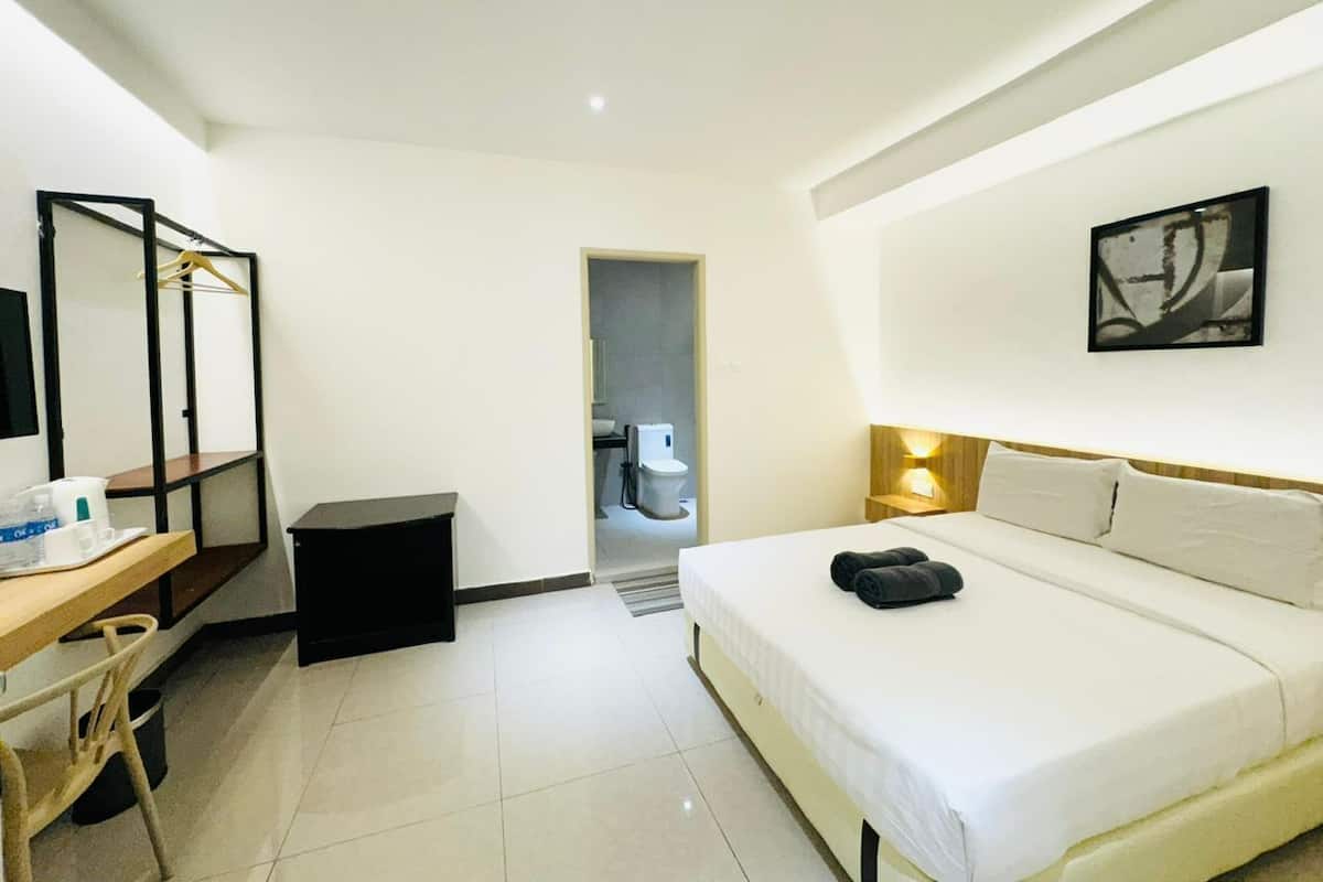 A hotel room with a bed, desk, chair, and a bathroom visible through an open door.