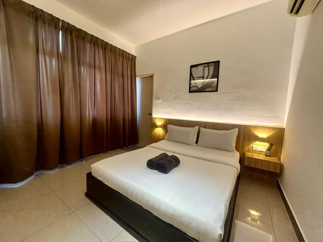 Una habitación de hotel con una cama grande, una mesita de noche con lámpara y un cuadro en la pared.
