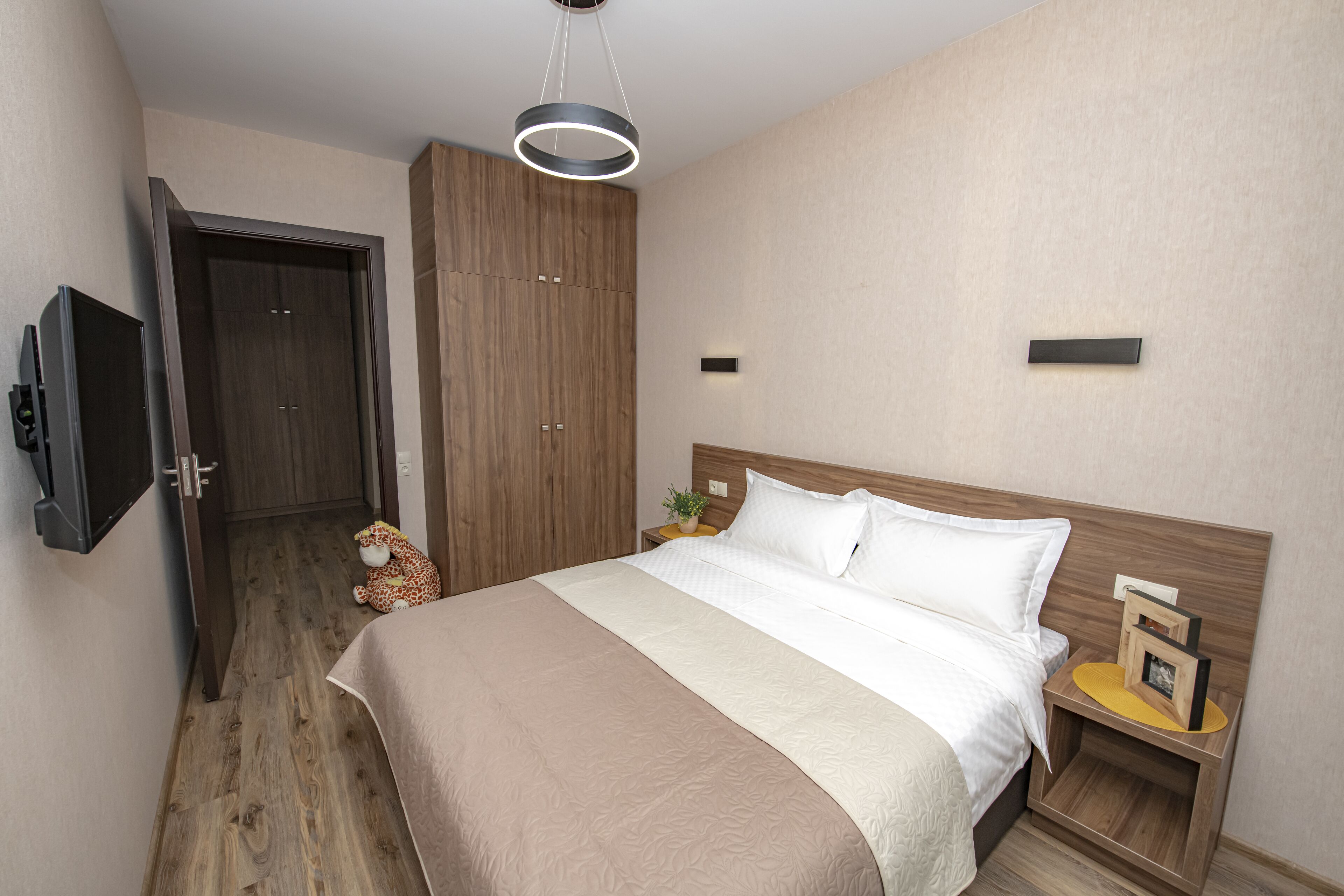 Ein Schlafzimmer mit Bett, Kleiderschrank, Nachttisch, Fernseher und Deckenleuchte.