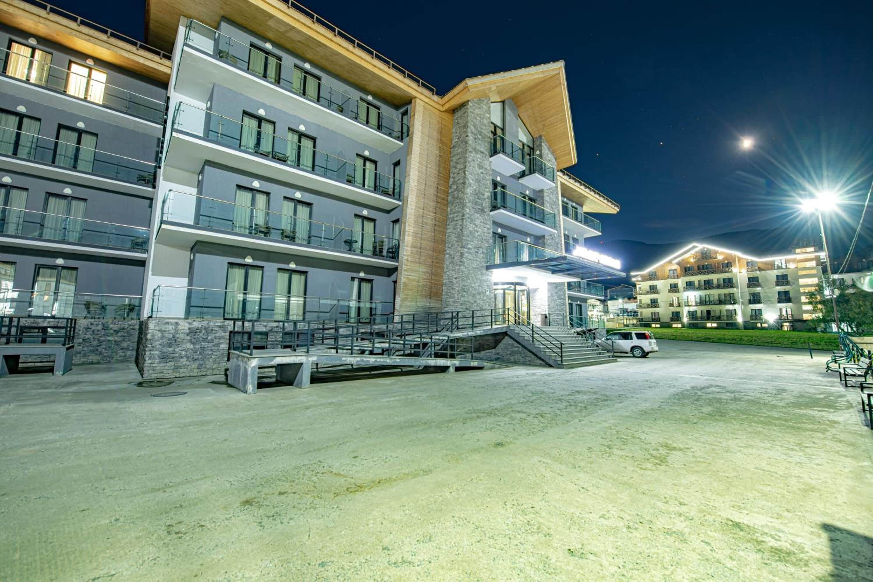 Um hotel de vários andares com varandas, uma escadaria central e área de estacionamento.