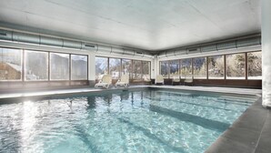 Ein Hallenbad mit klarem Wasser, großen Fenstern und Liegestühlen.