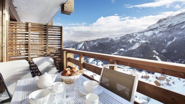 Ein Balkon mit Frühstückstisch, mit Blick auf eine verschneite Berglandschaft.