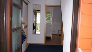 Un passadís estret amb una porta de fusta a l'esquerra, una finestra petita i una porta que condueix a una altra habitació.