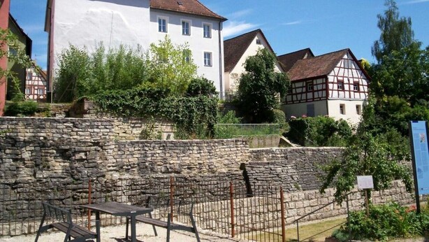 Edifici europeu tradicional amb mur de pedra i una banca de fusta al primer pla.