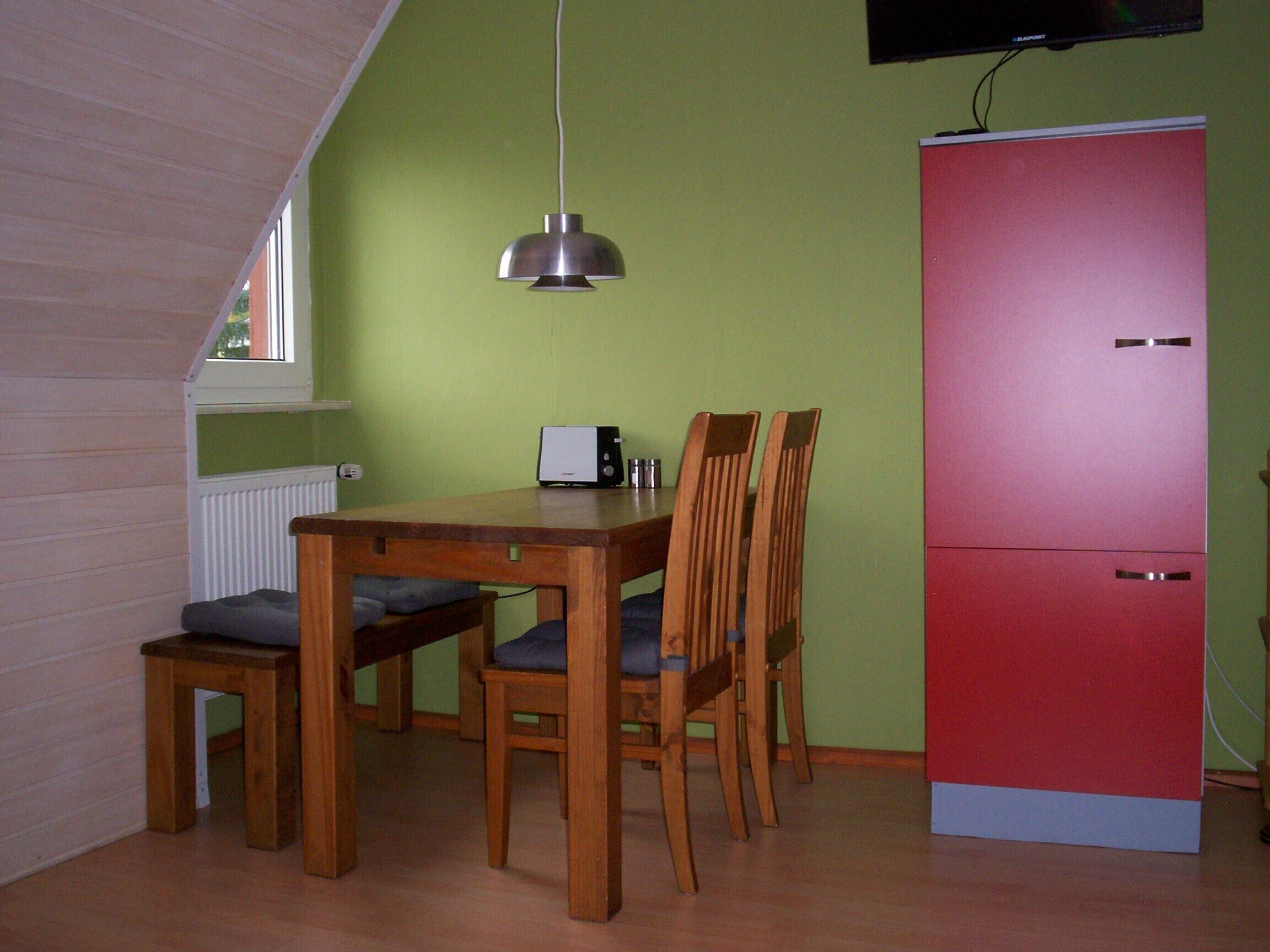 Un área de comedor con una mesa de madera, dos sillas, un banco, un refrigerador rojo y una lámpara en el techo.
