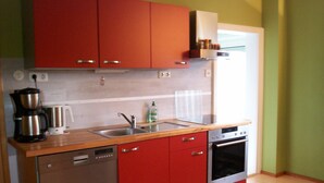 Una cuina compacta amb armaris vermells, un rentaplats d'acer inoxidable, un forn encastrat i un taulell de fusta.