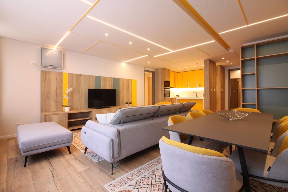 A modern living room with a sofa, ottoman, and a dining table with chairs.