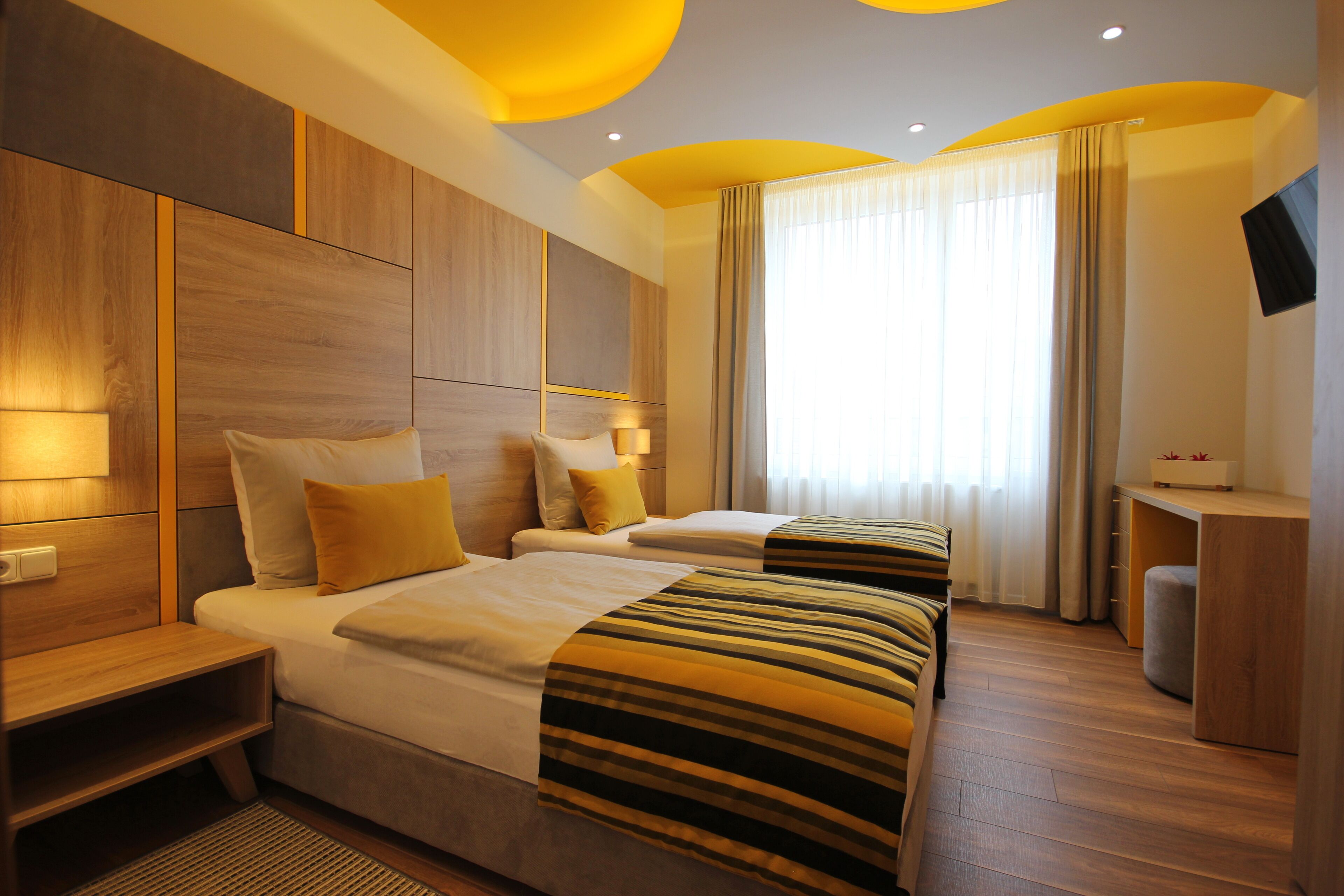 Une chambre d’hôtel avec deux lits, un bureau, une télévision et une grande fenêtre avec des rideaux.
