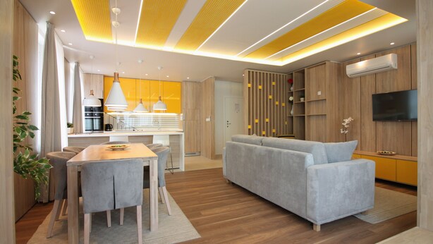Un salón moderno con un sofá gris, suelo de madera y una zona de comedor con mesa y sillas.