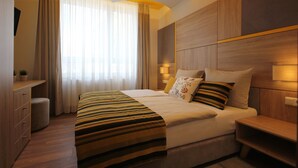 Una habitación de hotel moderna con una cama grande, cabecera de madera y un escritorio con lámpara.