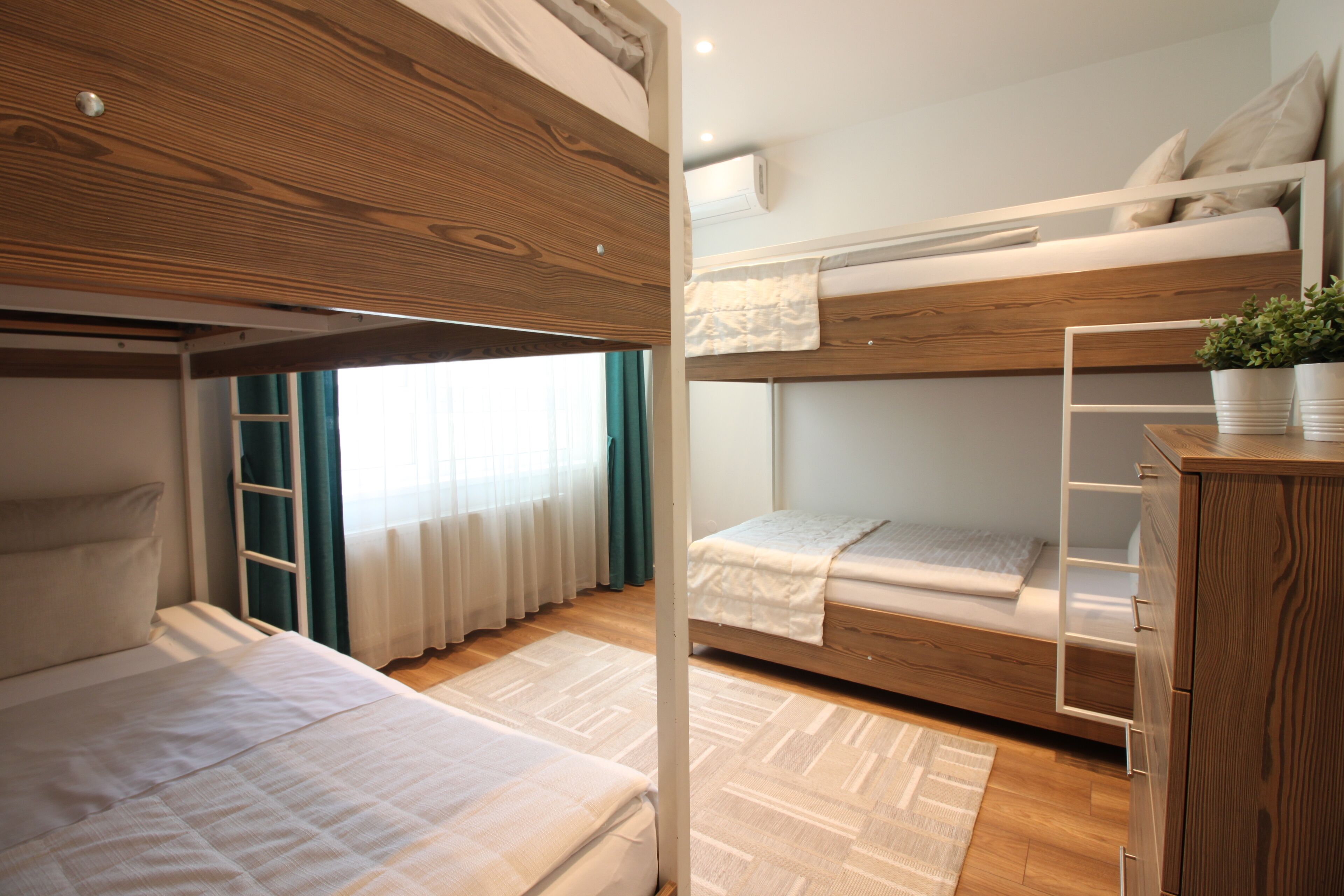 A bunk bed room with a wooden headboard, a small desk, and a potted plant.