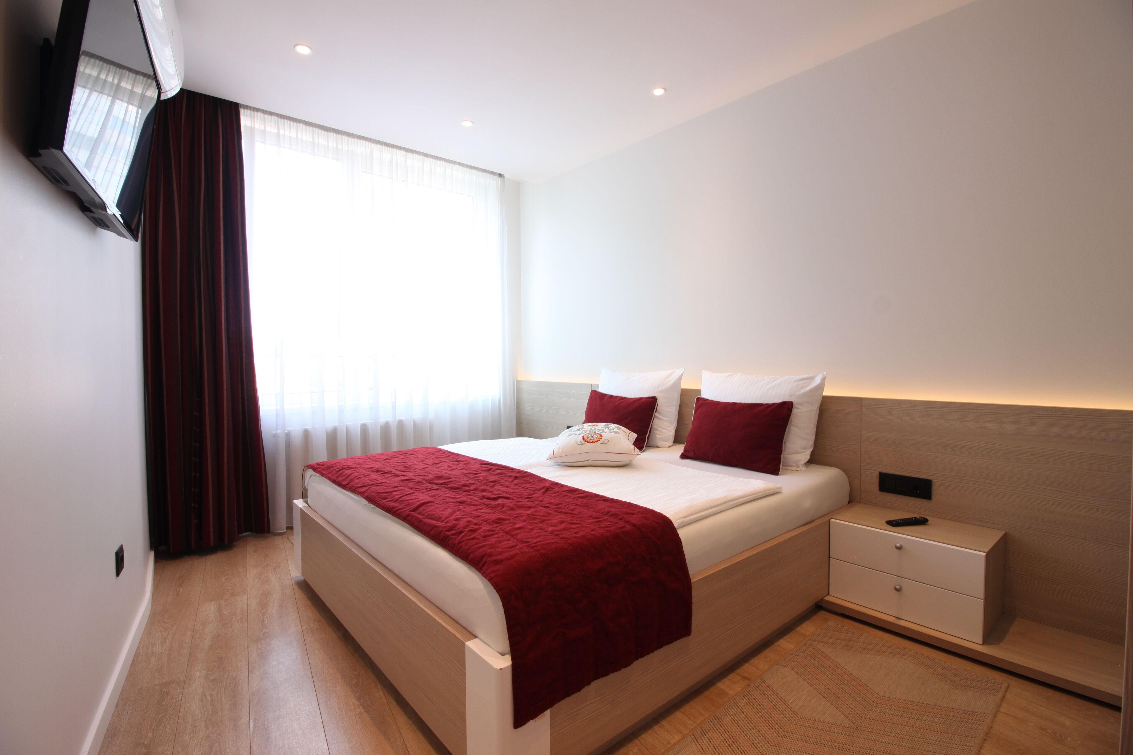 A modern hotel room with a large bed, a bedside table, and a flat-screen TV mounted on the wall.