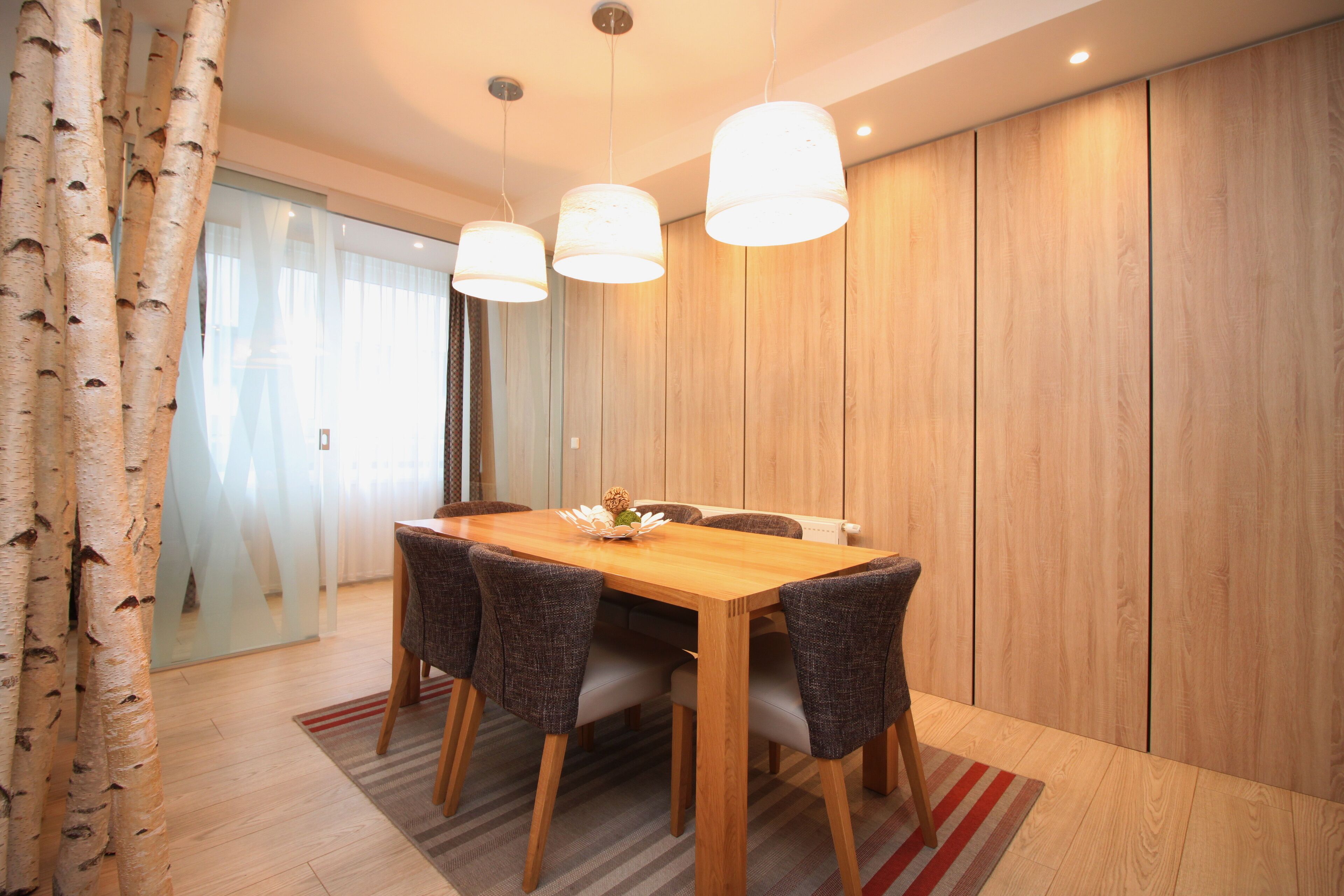 A dining area with a wooden table, four chairs, and three pendant lights.