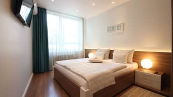 Un dormitorio moderno con una cama de madera, lámparas de noche, un televisor montado en la pared y un amplio ventanal con cortinas.