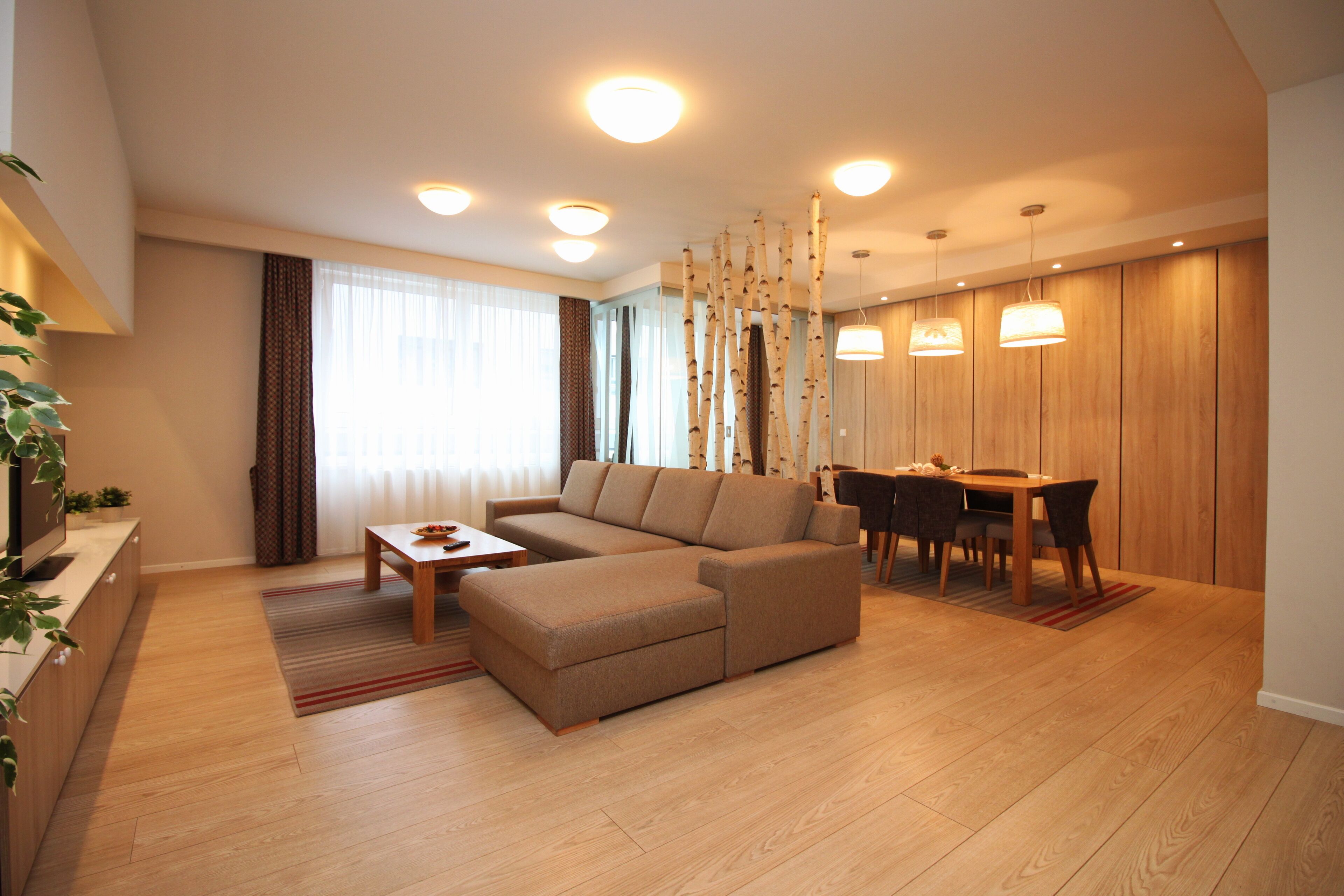 A modern living room with a sectional sofa, a dining table with chairs, and a TV on a wooden cabinet.
