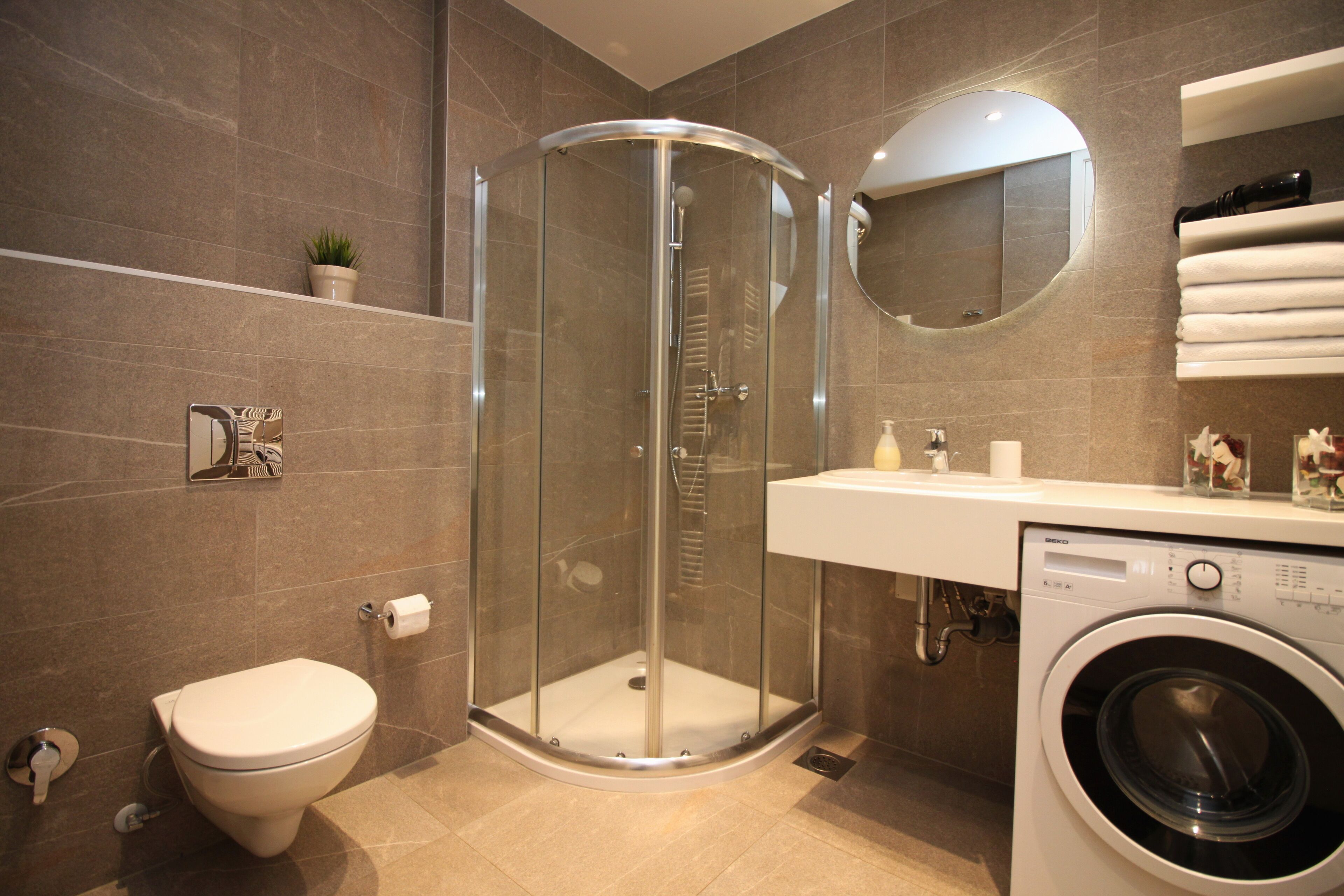 A modern bathroom with a glass-enclosed shower, a toilet, and a washing machine.