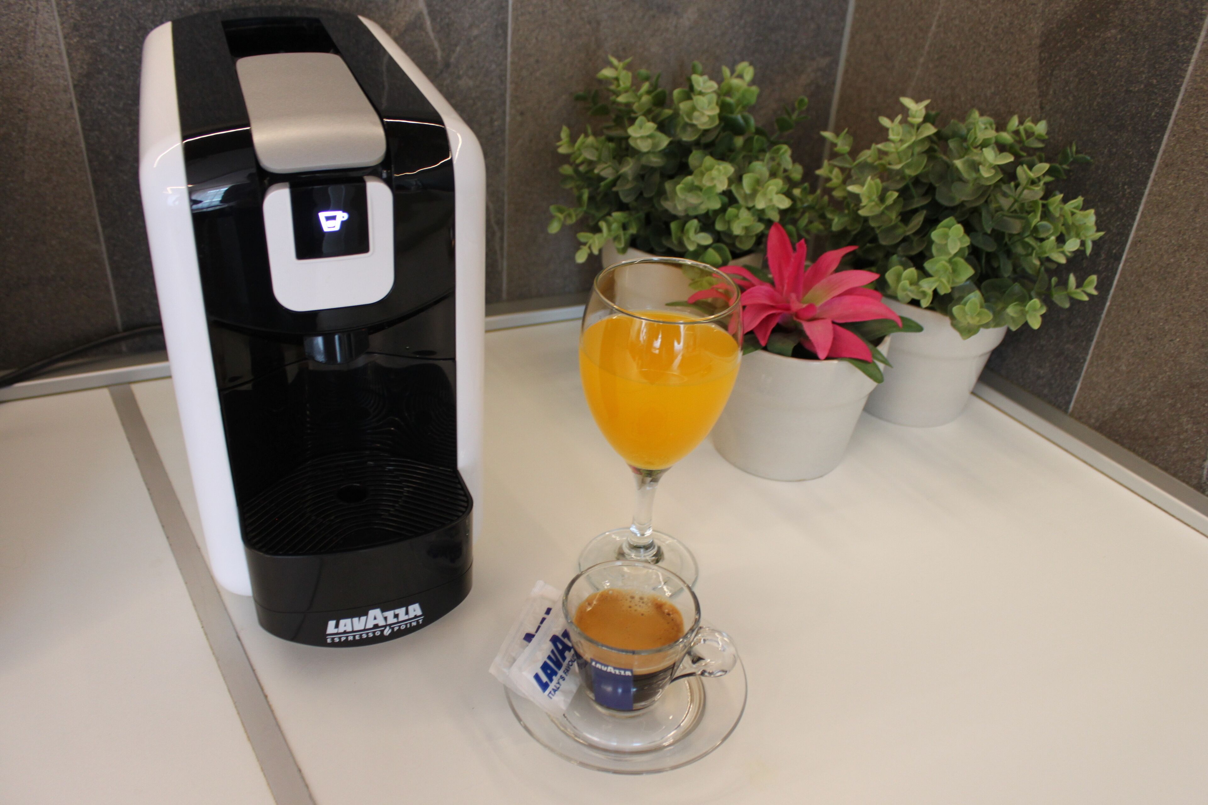 A coffee maker with a glass cup and a glass of orange juice on a countertop.