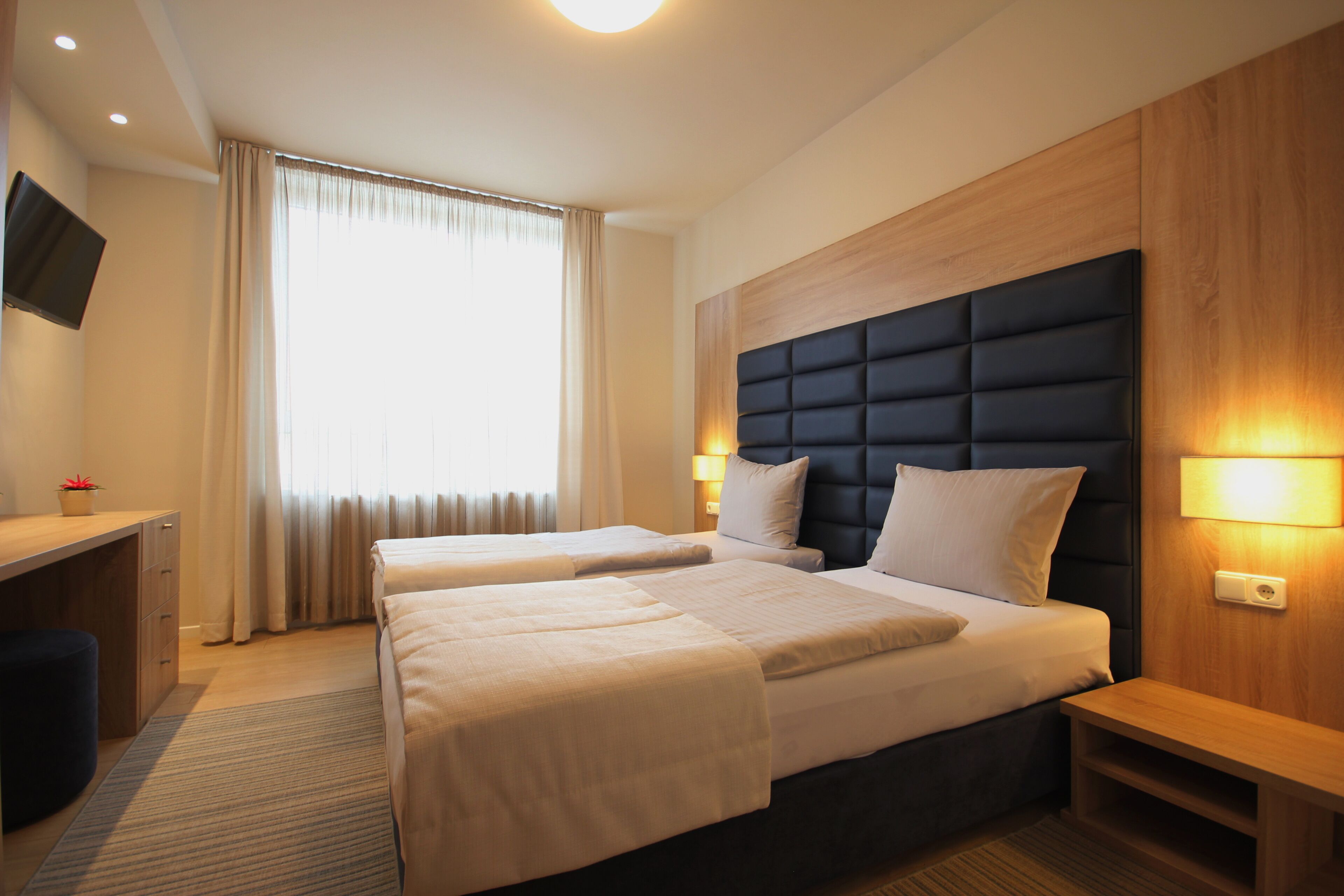 Habitación de hotel con dos camas, un escritorio, un televisor y una ventana con cortinas.