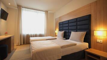 Habitación de hotel con dos camas, un escritorio, un televisor y una ventana con cortinas.