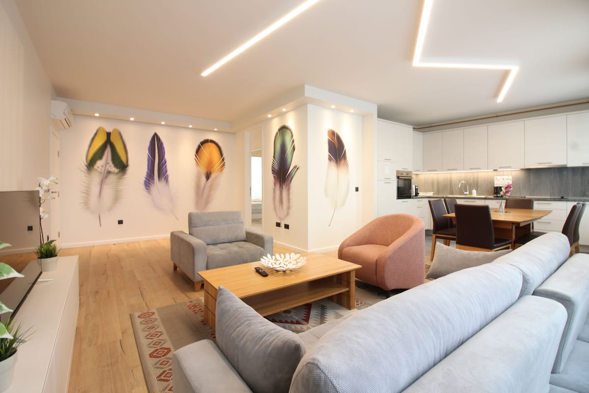 A modern living room with a sofa, armchairs, a coffee table, and a dining area with a table and chairs.