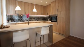 Cocina moderna con armarios de madera, encimera blanca, dos taburetes de bar e iluminación colgante.