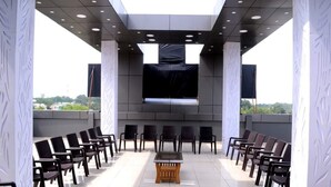 Un espace extérieur aménagé avec des chaises disposées en rangées, une table centrale et un grand écran à l’avant.