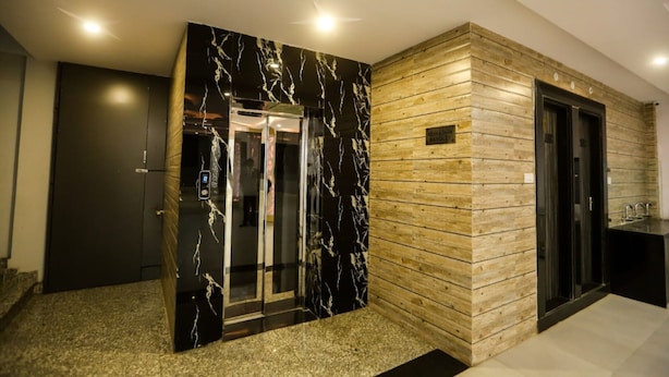 Un ascenseur moderne aux finitions en marbre, situé à côté d’un mur en bois sur lequel est apposée une plaque, et comprenant un petit coin cuisine.