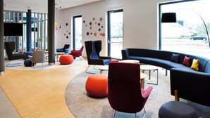 A modern lobby with a curved seating area, large windows, and a flat-screen TV mounted on the wall. - Holiday Inn Express Trier by IHG (Trier)