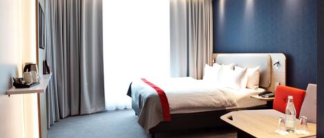A modern hotel room with a large bed, a desk, and a seating area.