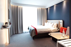 A modern hotel room with a large bed, a desk, and a seating area.