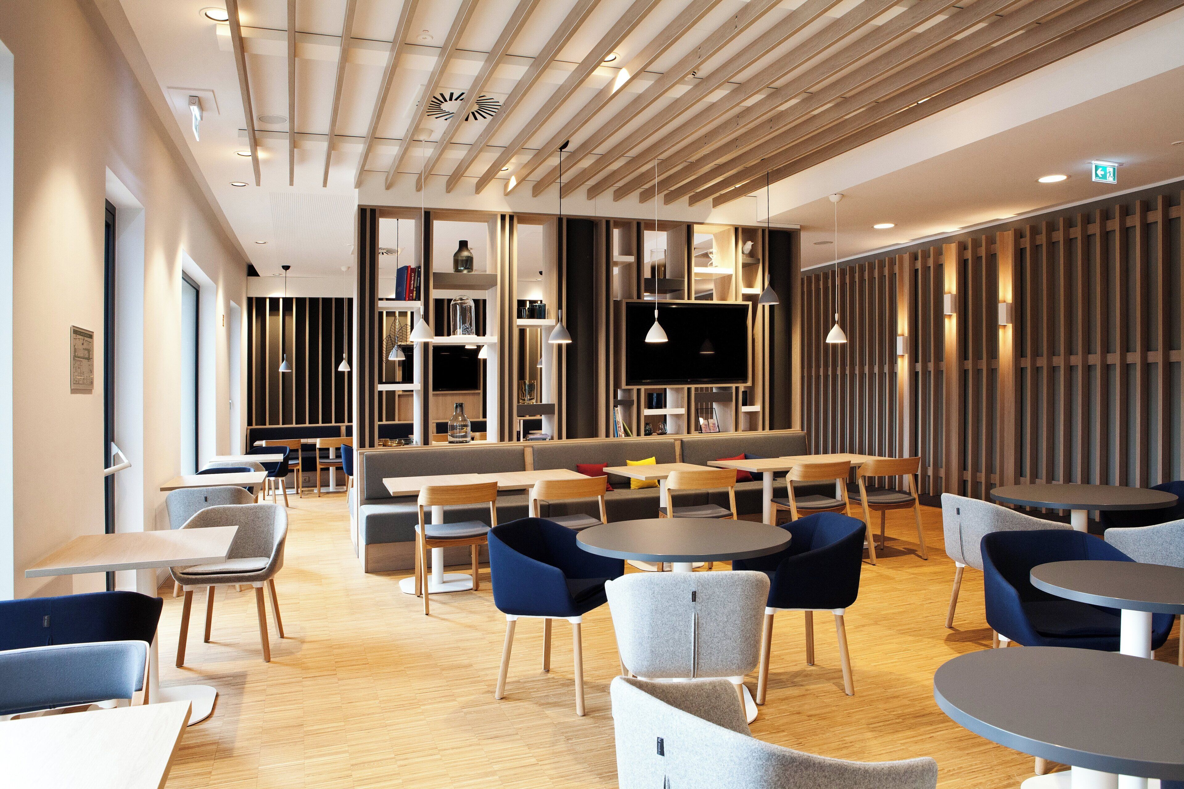 A modern interior with a mix of seating options including tables and booths, a flat-screen TV mounted on a wall, and a variety of lighting fixtures.