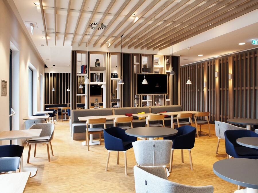 A modern interior with a mix of seating options including tables and booths, a flat-screen TV mounted on a wall, and a variety of lighting fixtures.