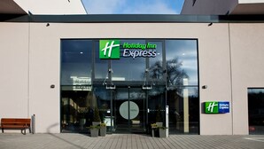 Edificio de Holiday Inn Express con fachada de vidrio, un banco fuera y plantas en macetas al frente.