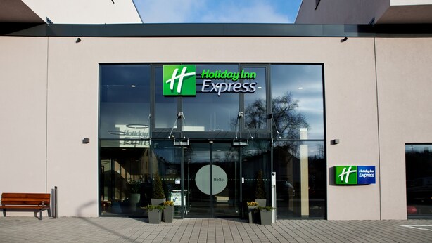A Holiday Inn Express building with a glass facade, a bench outside, and potted plants in front. - Holiday Inn Express Trier by IHG (Trier)
