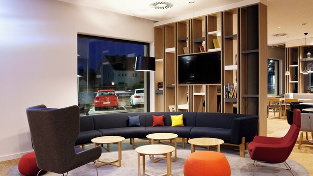 A modern living room with a sectional sofa, round tables, and a large TV. - Holiday Inn Express Trier by IHG (Trier)