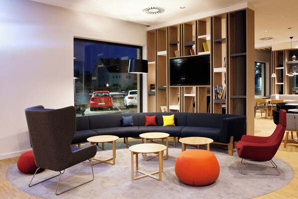 A modern living room with a sectional sofa, round tables, and a large TV. - Holiday Inn Express Trier by IHG (Trier)