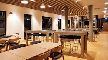 A modern dining area with wooden tables and chairs, a high ceiling with wooden slats, and pendant lighting.