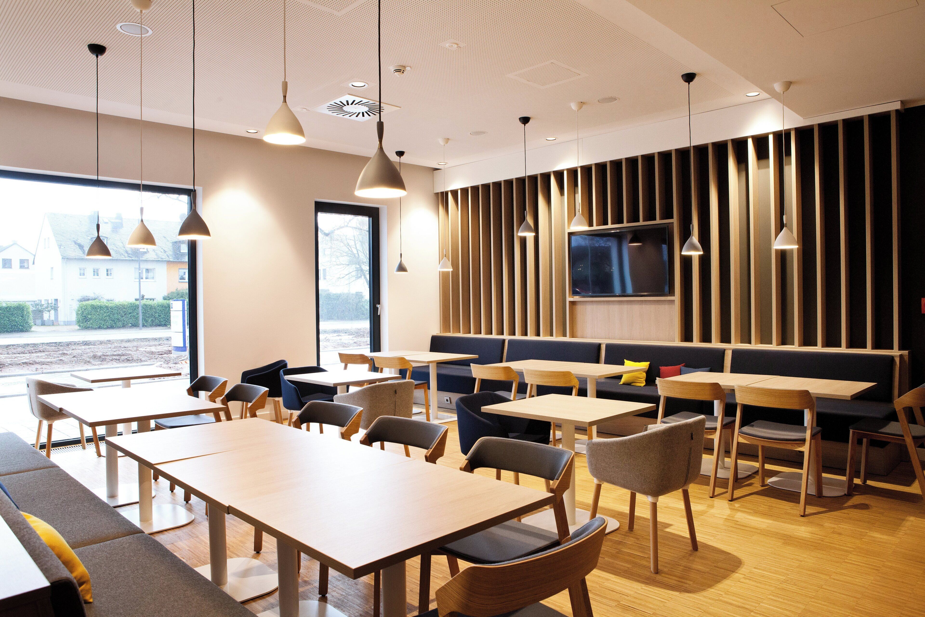 A modern dining area with tables and chairs, a large window, and a television on the wall.