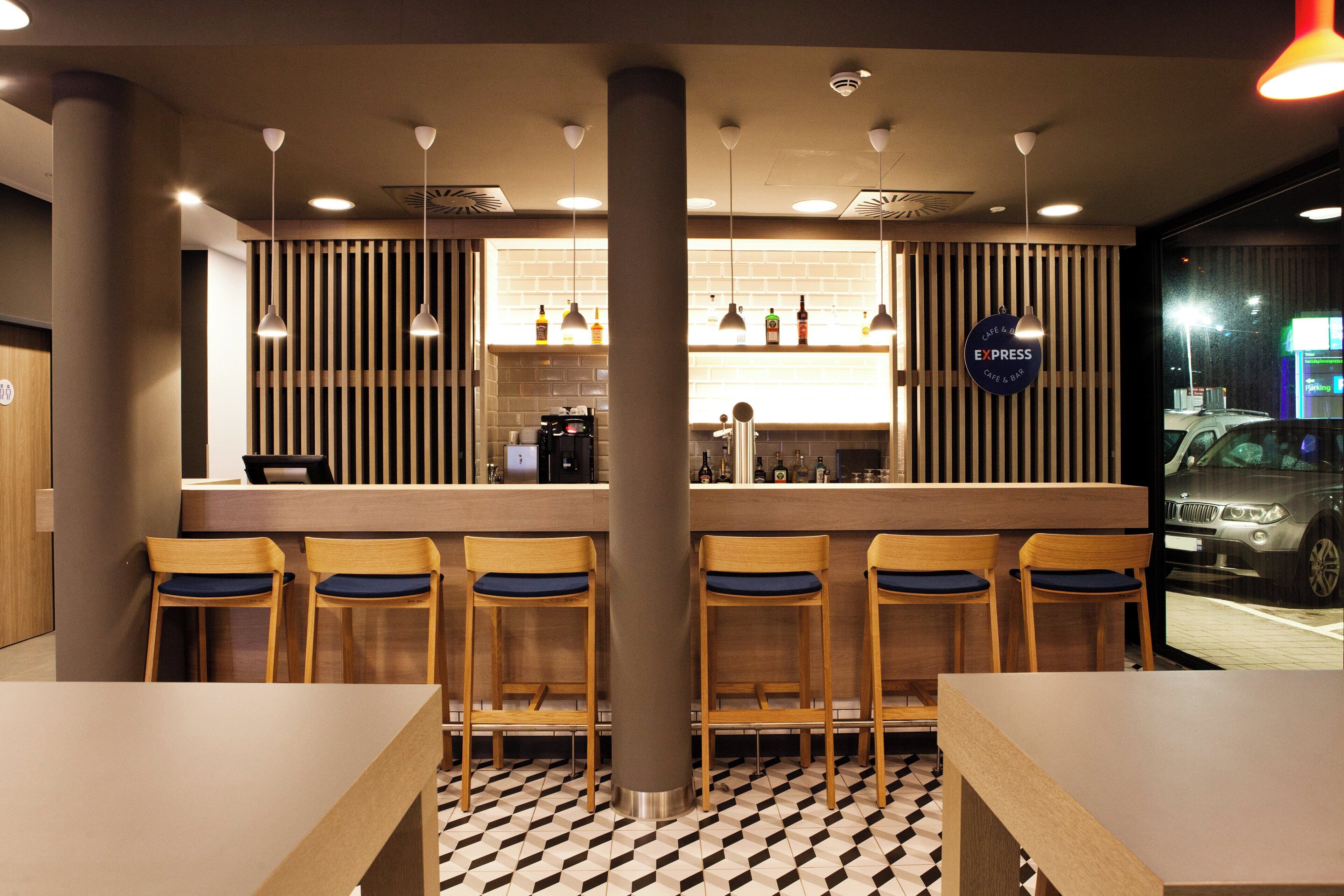 Een moderne barruimte met houten barkrukken, een toonbank met een koffiemachine, en een bord waarop staat dat het een Express Café & Bar is.