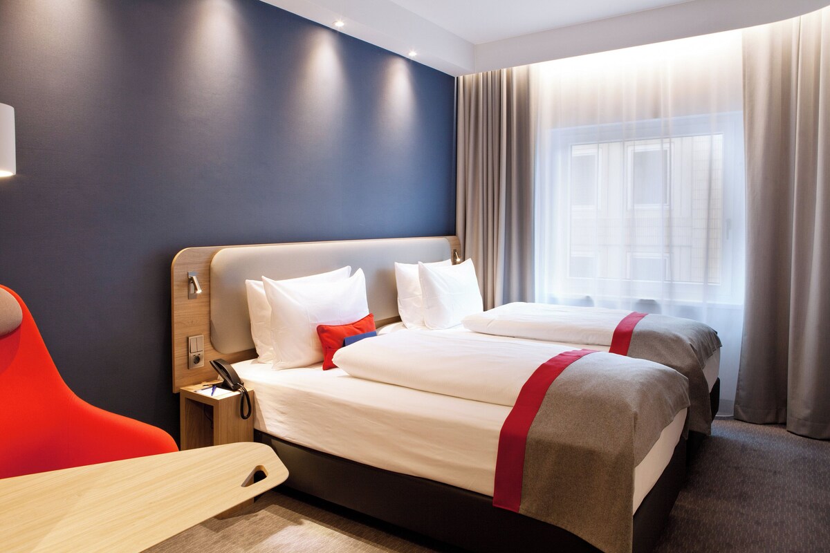 A hotel room with two beds, a desk, a chair, a telephone, and a window with curtains.