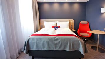 Ein Hotelzimmer mit einem Bett, einem roten Sessel, einem kleinen Tisch und einer Wandlampe.