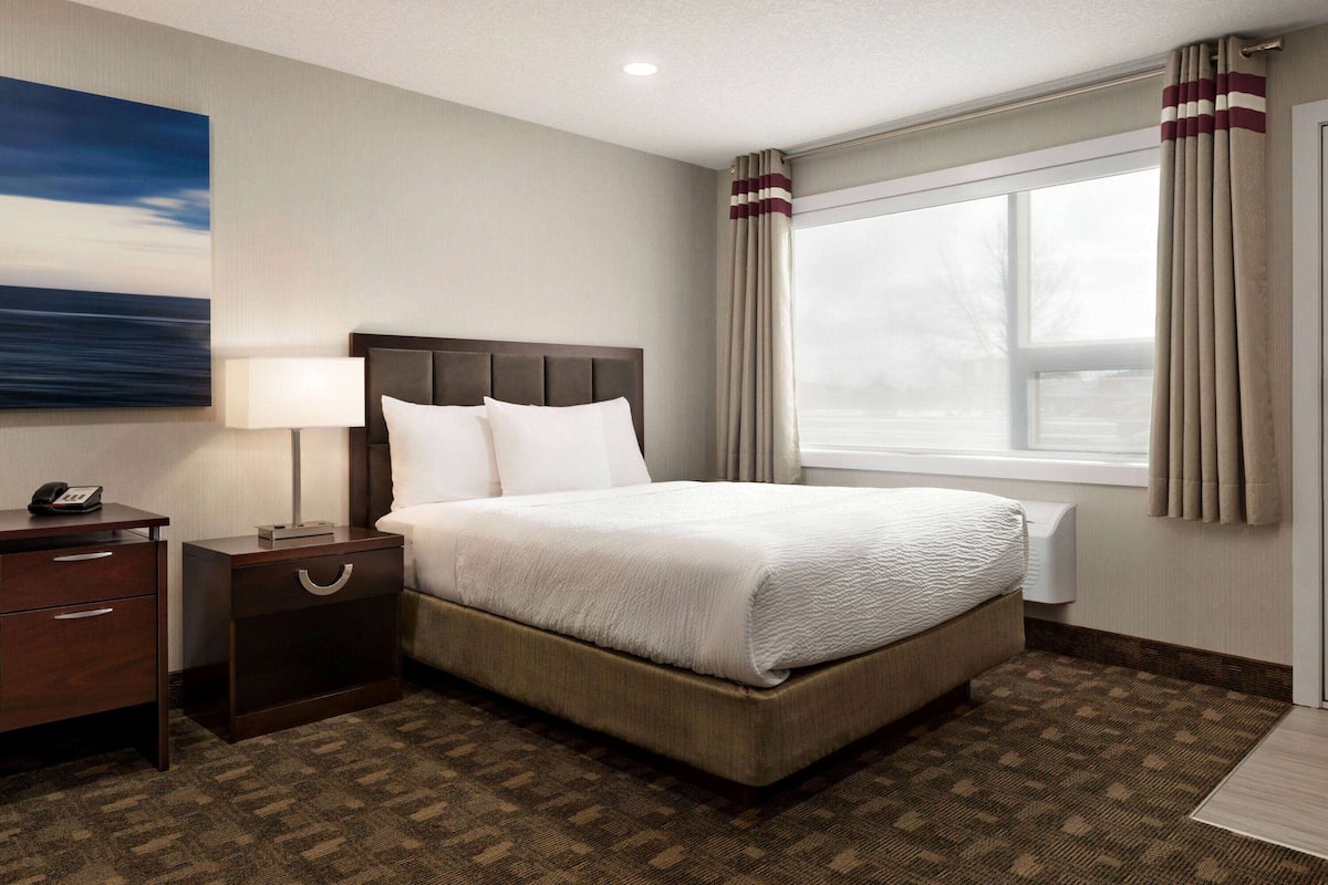 A hotel room with a large bed, a nightstand with a lamp, a telephone, and a painting on the wall.