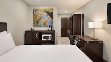 Una habitación de hotel con una cama, un escritorio con una silla, un microondas, un teléfono y un cuadro de hojas otoñales.