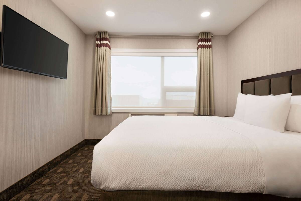 A hotel room with a large bed, a flat-screen TV mounted on the wall, and a window with curtains.